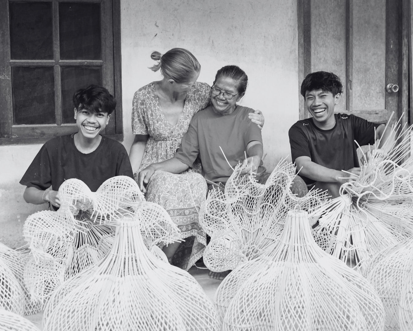 Artisans smiling as they sit with founder Anna, and weave lights for Lighthouse Lane