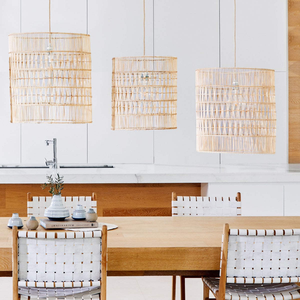 Rattan pendant light shade. Lifestyle-photo-showing-3-cylindrical-shaped-natural-rattan-light-shades-over-a-timber-dining-table