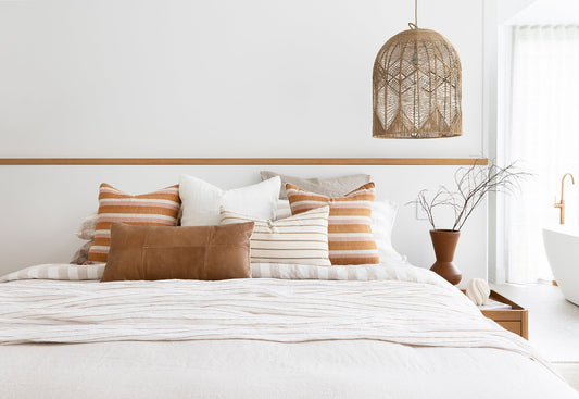 Airlie feature pendant light hangs above a bedside table. The bedlinen on the bed is mostly white with some natural coloured accent cushions.