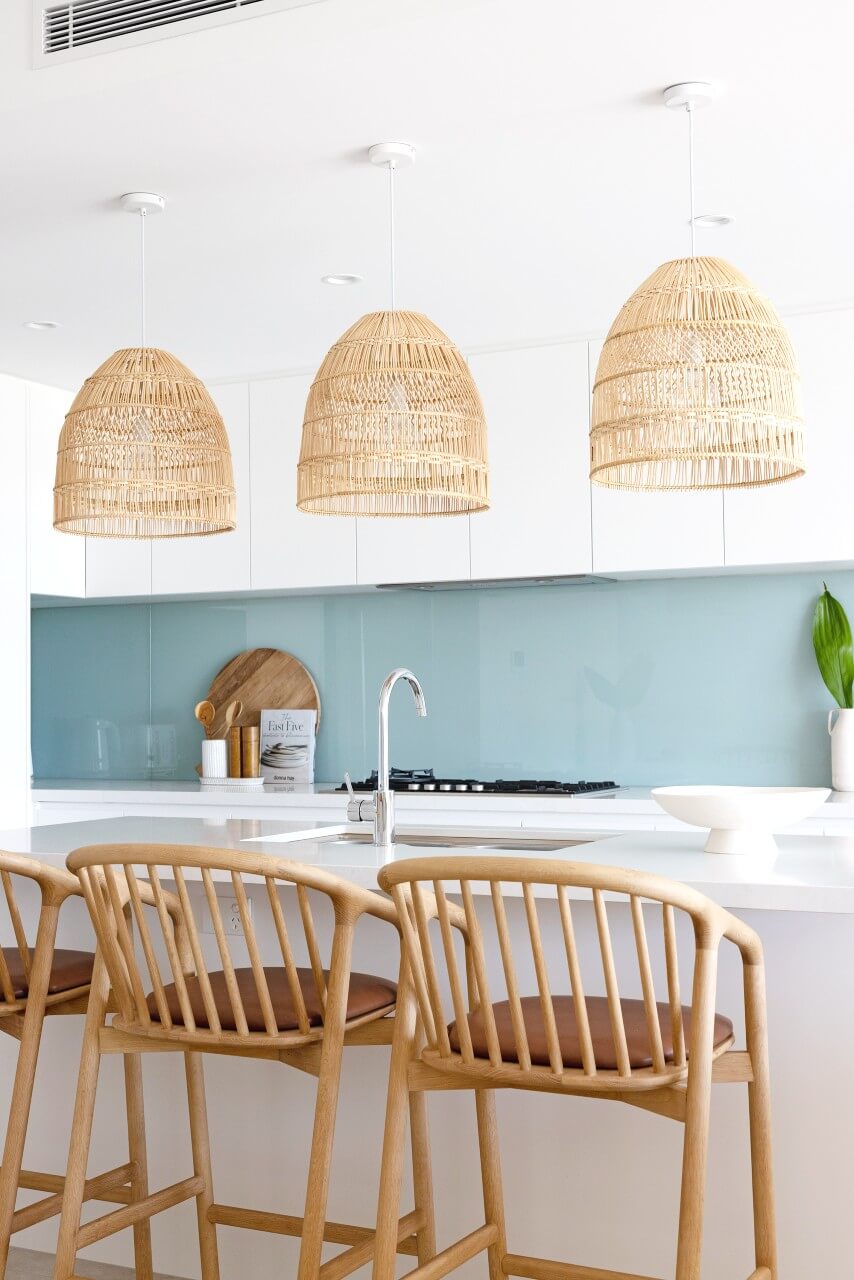 Three Flinders natural kitchen pendant lights hang above a white stone island bench. The white kitchen has a beautiful sea blue glass backsplash.