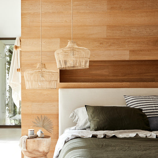 Henley Rattan natural pendant lighting hangs above a timber stool next to a bed dressed in olive linen bedsheets.