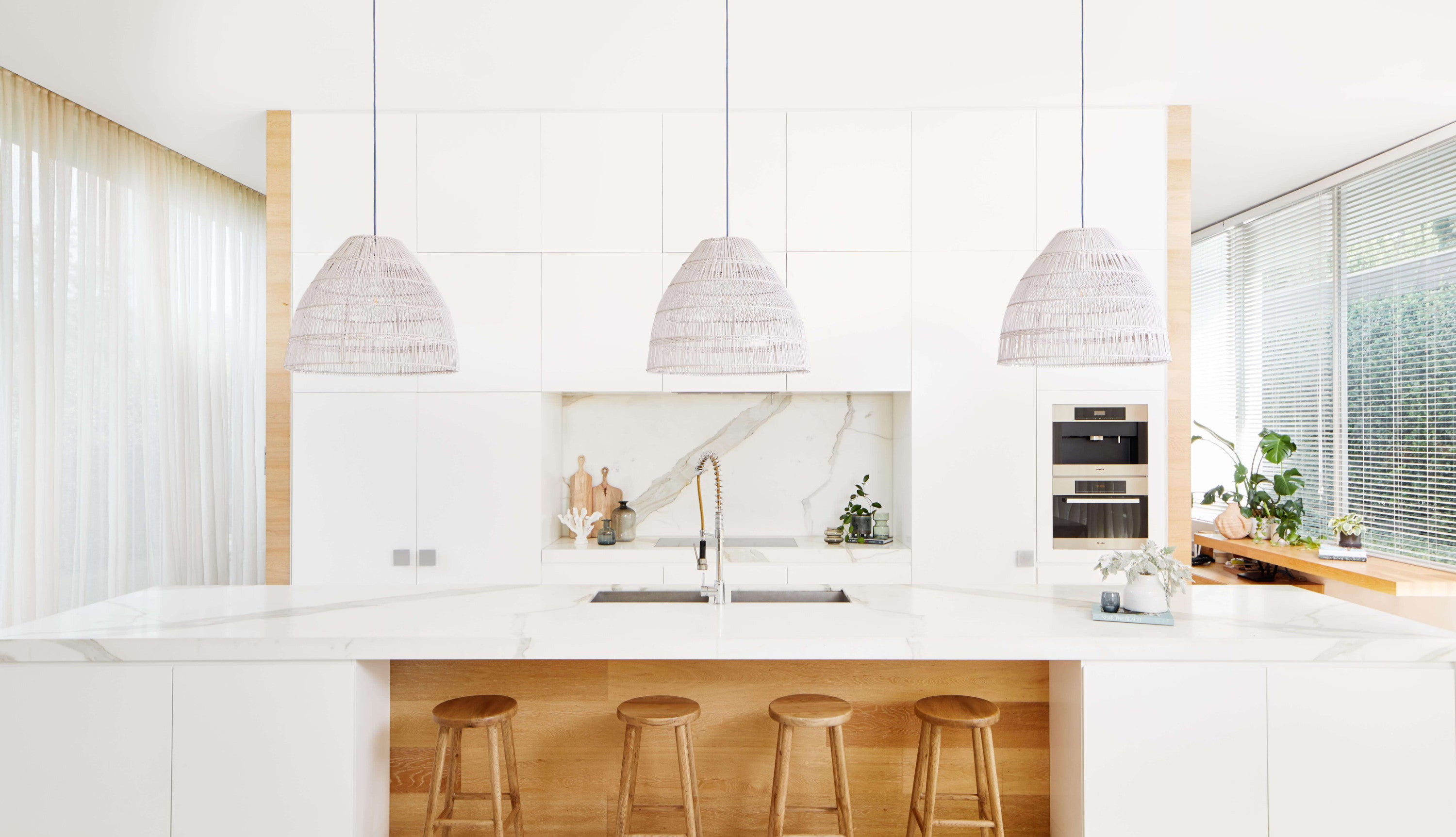 Three white Marlo sustainable pendant lights hang over a large marble kitchen island bench.