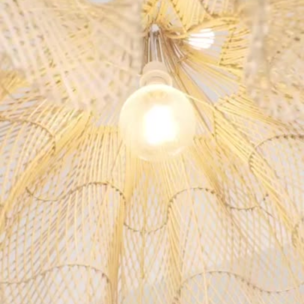 A close-up of a woven ceiling light fixture made from natural beige raffia or straw fibers, with a glowing warm white bulb at the center.