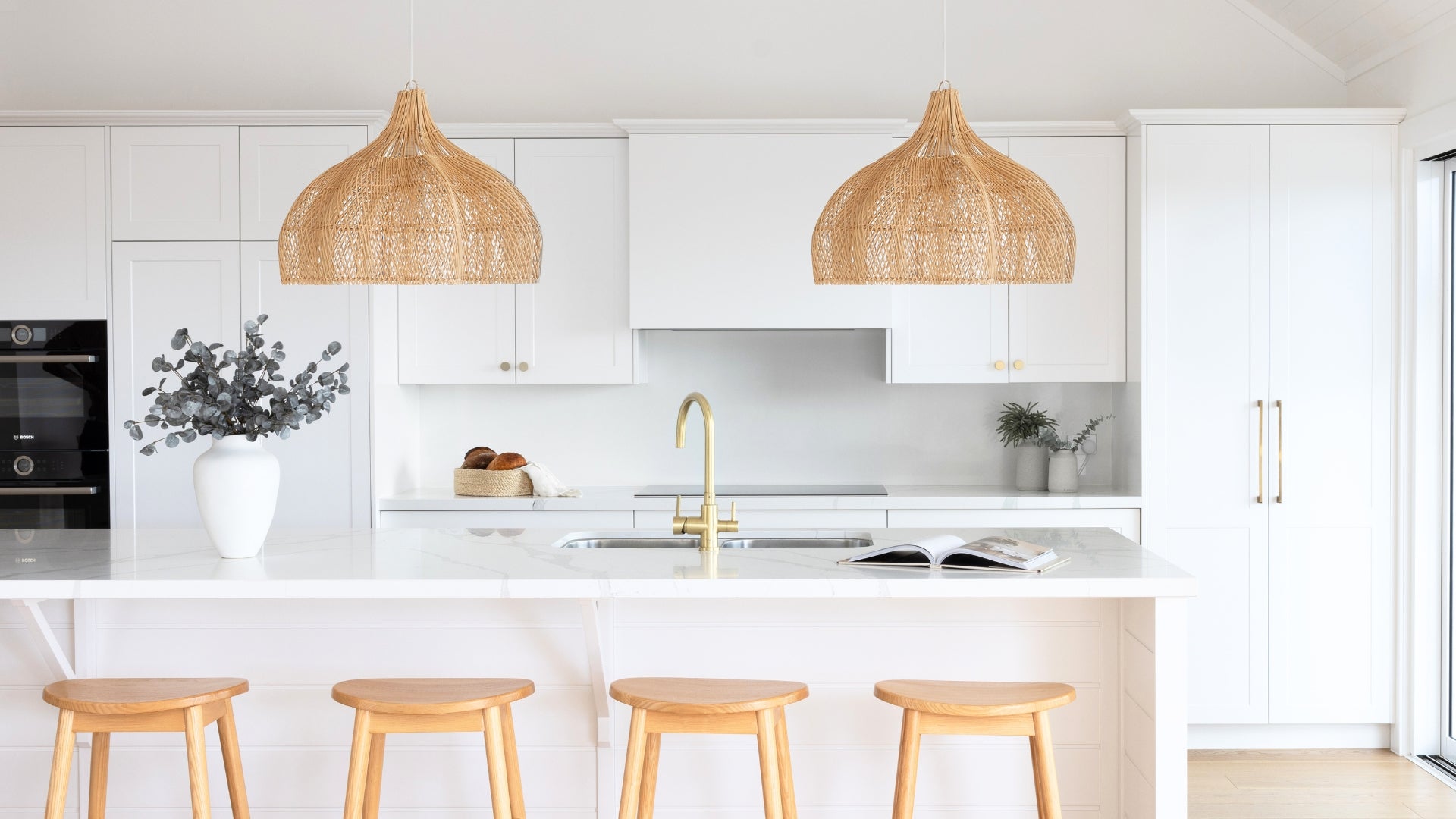 A bright, modern kitchen with white cabinetry, a white marble island, two woven wicker pendant lights, and four wooden bar stools.