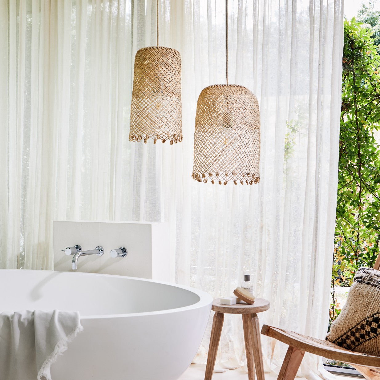 Luxurious-lifestyle-photo-of-Natural-coastal-style-lighting-showing-a-small-and-a-medium-borneo-basket-light-shade-with-open-weave-and-ring-detail-at-the-bottom-hanging-above-a-free-standing-bath-with-teak-side-table-and-teak-chair