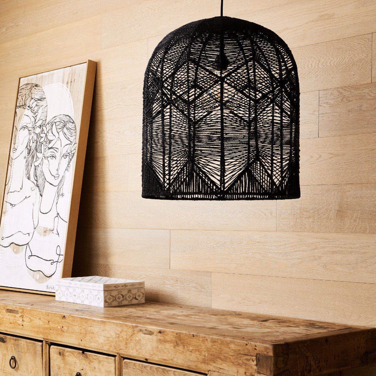 Seagrass pendant light black. hangs over a recycled elm chest. dome shaped with a diamond pattern.