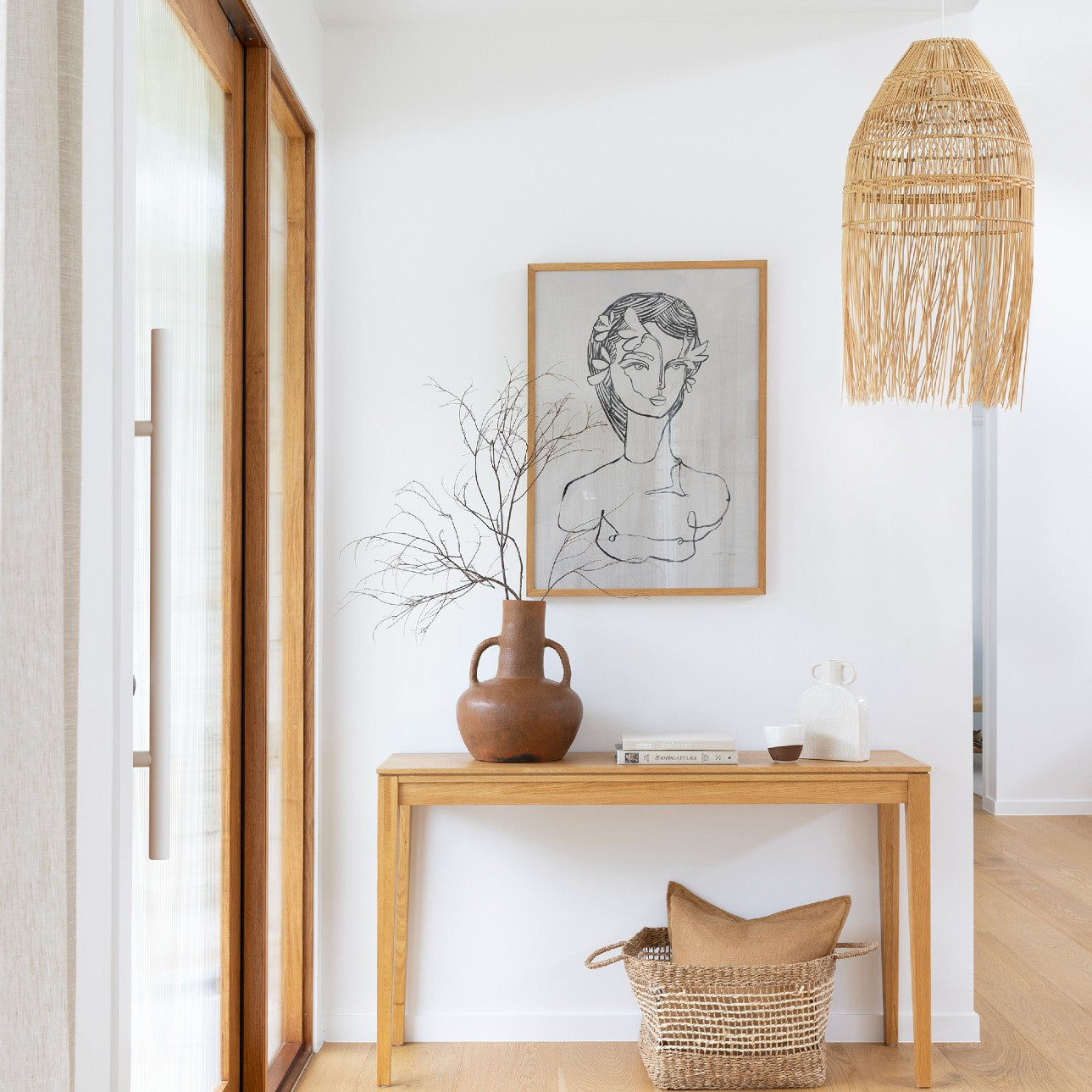boho lighting. this rattan pendant light shade hangs above a side table next to an artwork of a woman.
