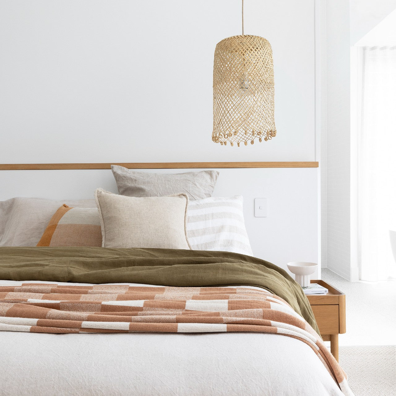 Rattan pendant light with ring details at the bottom. shown as a bedisde pendant hanging above a beuaitfully made bed with olive green and rust coloured bed linen.