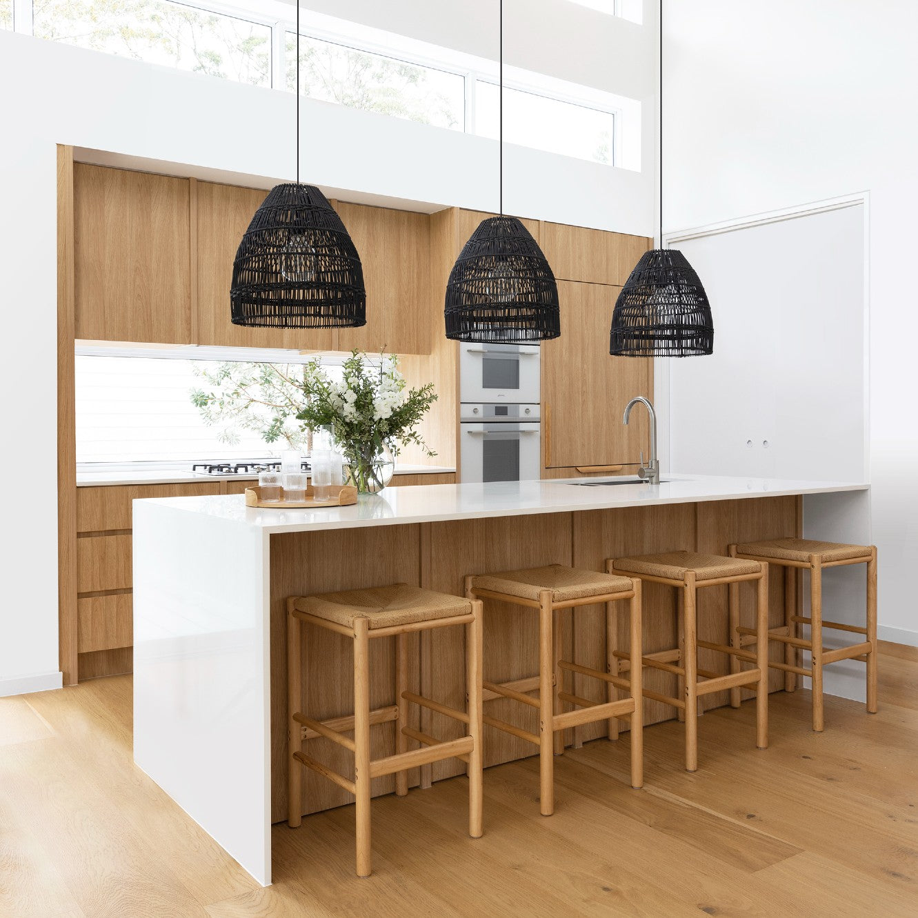 black rattan pendant lights. 3 black rattan light shades hang in an oak and white kitchen which is filled with natural light.