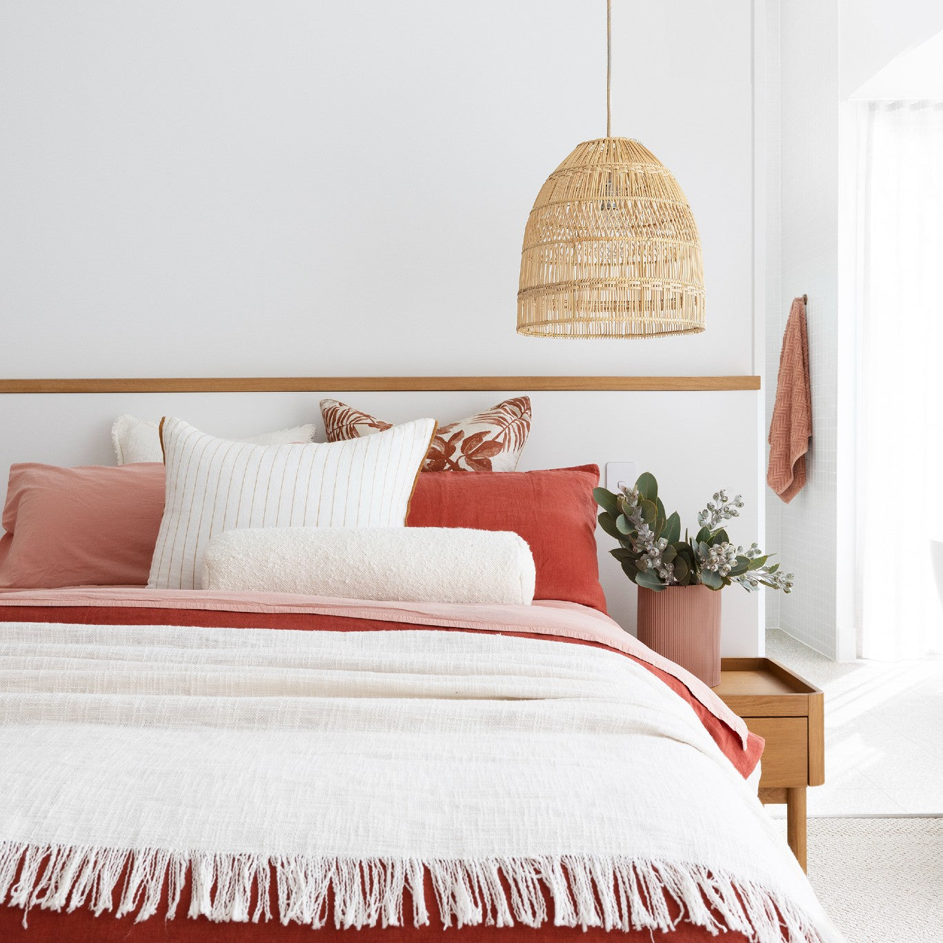 Rattan coastal pendant light. hanging above a bed dressed with dusty pink and rusty red bed linen with a cream throw.